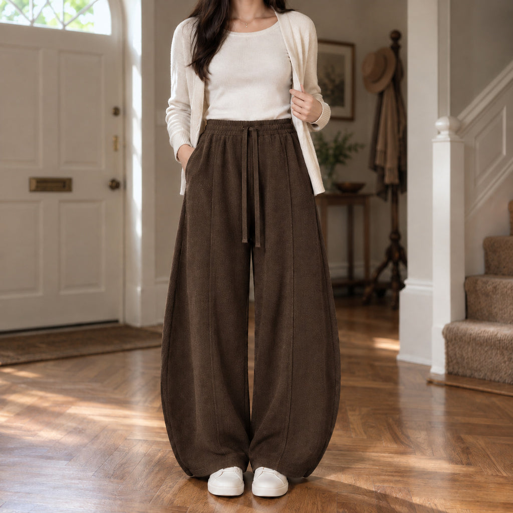 Ormsby Ribbed Wide Leg Trousers — Dark brown ribbed wide-leg pants worn by a model in a lived-in panelled room.