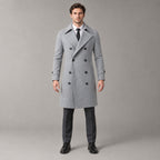 Norbury Cotton Blend Trench Coat — Light gray double-breasted trench coat worn by a model against a pale stone studio backdrop.