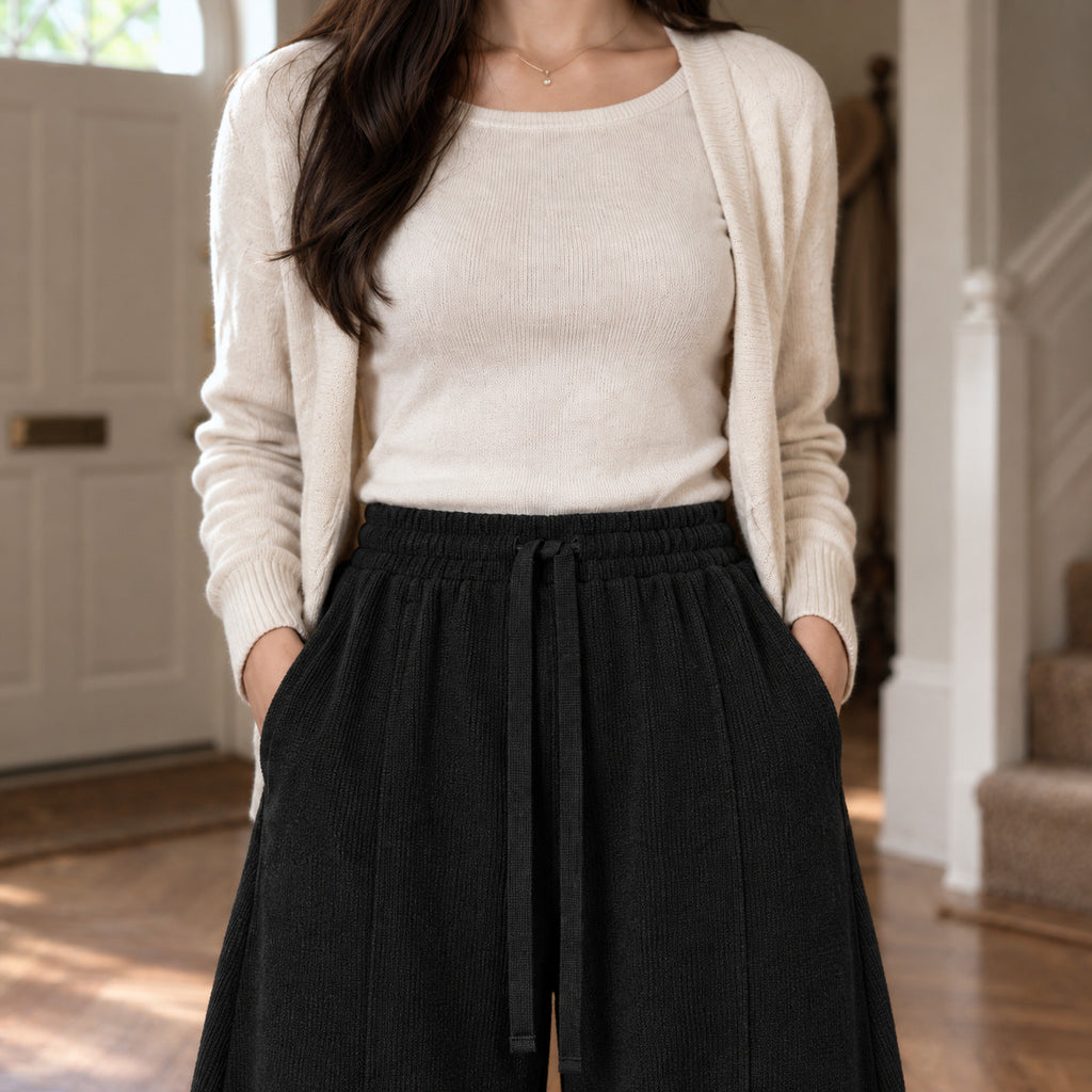 Ormsby Ribbed Wide Leg Trousers — Black ribbed wide-leg pants worn, cropped from the shoulders to the waist to show the elastic waistband and ribbed knit.
