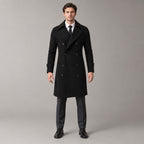 Norbury Cotton Blend Trench Coat — Black double-breasted trench coat worn by a model against a pale stone studio backdrop.
